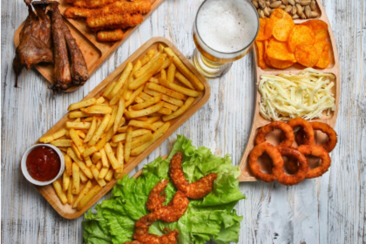 A wooden table topped with a variety of unhealthy food items, including french fries, onion rings, and chips